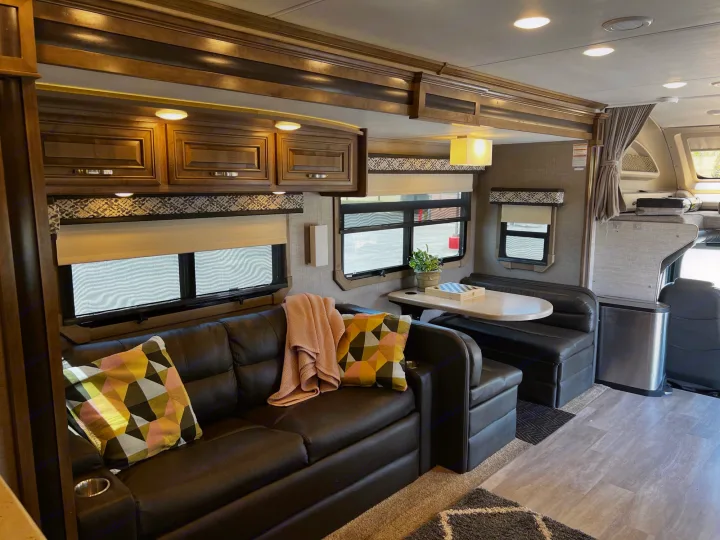 An RV rental's inviting interior, showcasing a comfy sofa, dinette, and wooden overhead cabinets.. Jayco Seneca 2021
