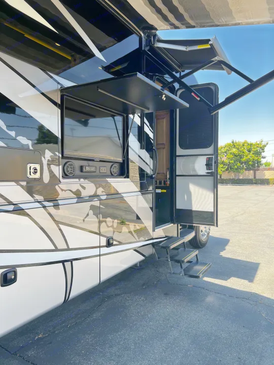 This RV rental offers an outdoor entertainment setup with a pull-out TV, speakers, and a large awning above its entry steps.. Jayco Seneca 2021