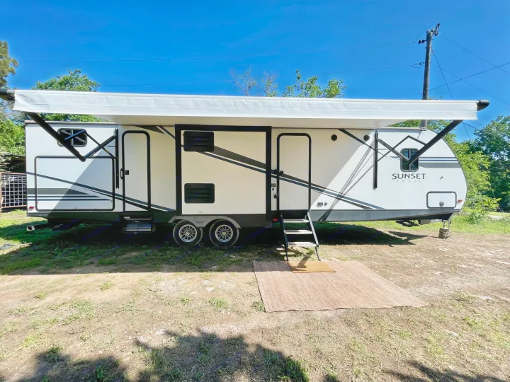 Experience outdoor adventure with this Sunset Trail rv rental. A white travel trailer with an awning under a sunny blue sky.. Crossroads RV Sunset Trail Super Lite 2019