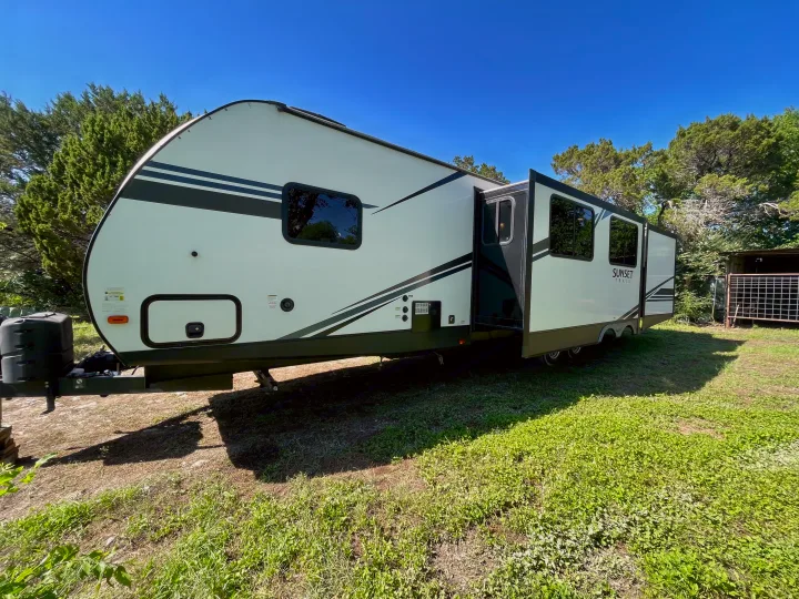 This white travel trailer RV rental, with an extended slide-out, is parked on grass and ready for your next outdoor vacation.. Crossroads RV Sunset Trail Super Lite 2019
