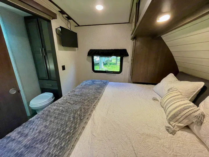 Cozy RV rental bedroom featuring a comfortable bed, compact toilet, wall-mounted TV, and window for your travels.. Crossroads RV Sunset Trail Super Lite 2019