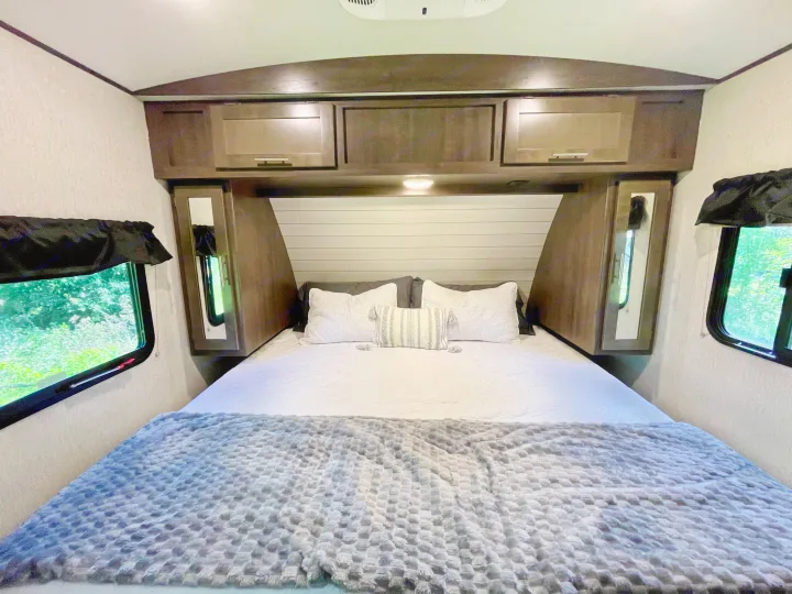 Cozy RV rental bedroom with ample overhead storage, soft bedding, and side windows for a comfortable stay.. Crossroads RV Sunset Trail Super Lite 2019