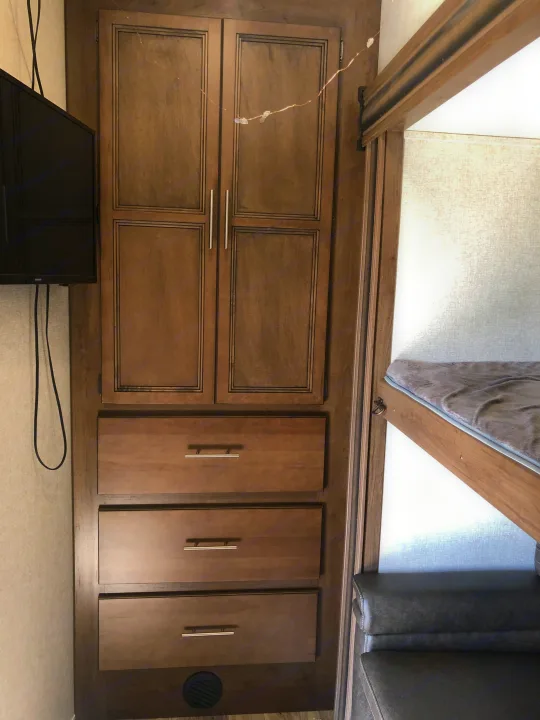 RV rental: Wooden cabinet with upper doors, lower drawers. TV left, bunk bed & upholstered seating right. Functional, cozy space.. Keystone RV Cougar 2020