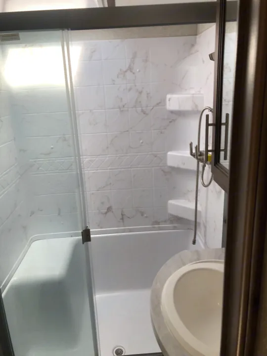 Modern RV rental bathroom featuring a shower-tub combo, sliding glass door, and partial view of a sink.. Keystone RV Cougar 2020