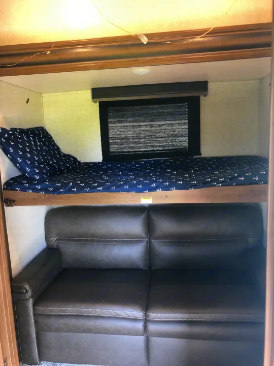 RV rental interior featuring a bunk bed with anchor bedding over a dark sofa, a cozy sleeping/lounge area.. Keystone RV Cougar 2020