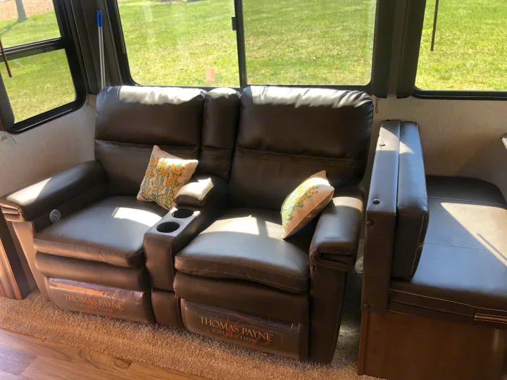 Cozy RV rental interior: A 'Thomas Payne Collection' reclining loveseat with cup holders offers comfortable seating by large windows.. Keystone RV Cougar 2020