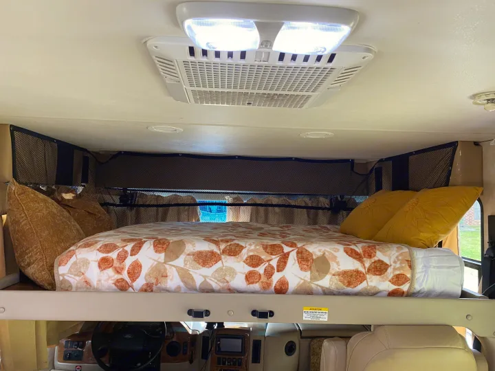 Cozy motorhome RV rental overhead bunk bed, with leaf-patterned bedding, pillows, and safety net.. Thor Hurricane 2014