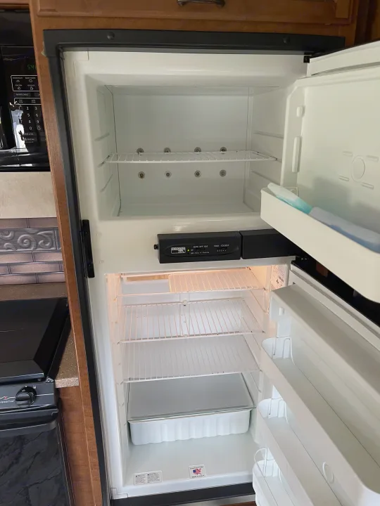 Empty Norcold refrigerator in an rv rental. This clean RV fridge interior shows shelves and door storage. Microwave nearby.. Thor Hurricane 2014