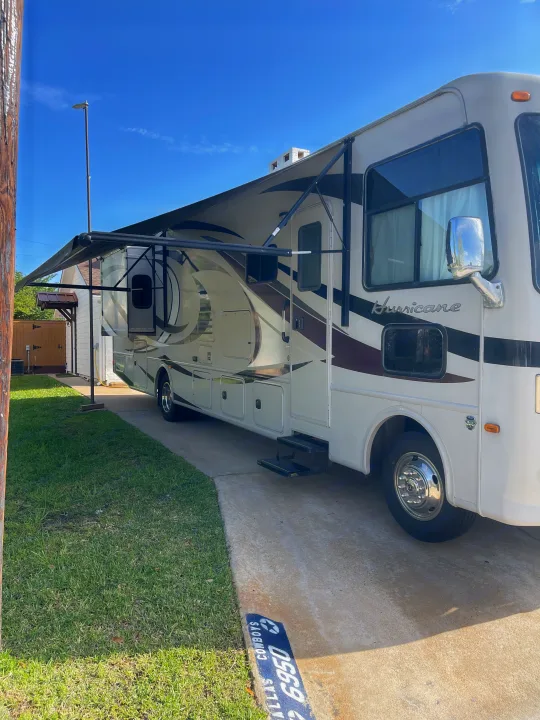 White Hurricane RV rental, a motorhome with an extended awning, parked on a sunny driveway.. Thor Hurricane 2014