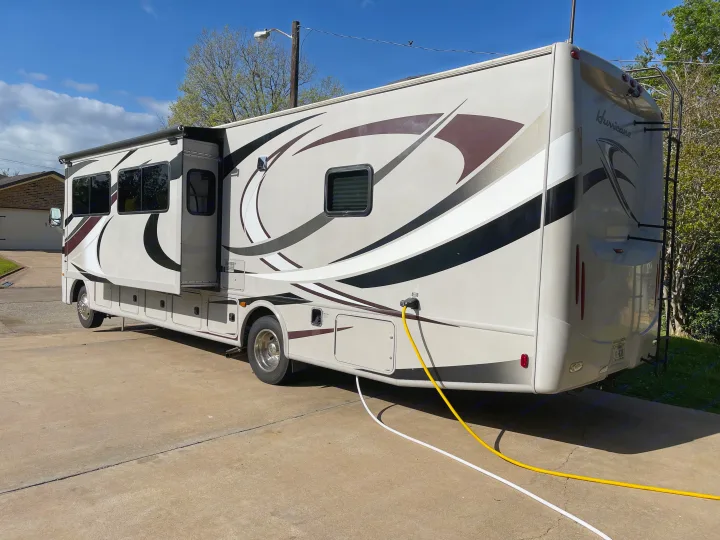Spacious RV rental, beige with graphics, parked on a concrete drive with slides extended & hookups connected.. Thor Hurricane 2014