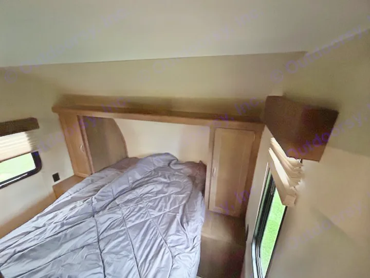 RV rental bedroom: a compact space with a bed, overhead storage, windows, and mounted TV.. Gulf Stream Trailmaster 2018