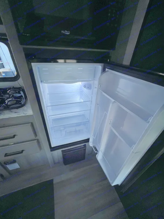 Empty, bright refrigerator in an RV rental kitchen, with microwave and stove visible.. Keystone RV Hideout Sport 2024