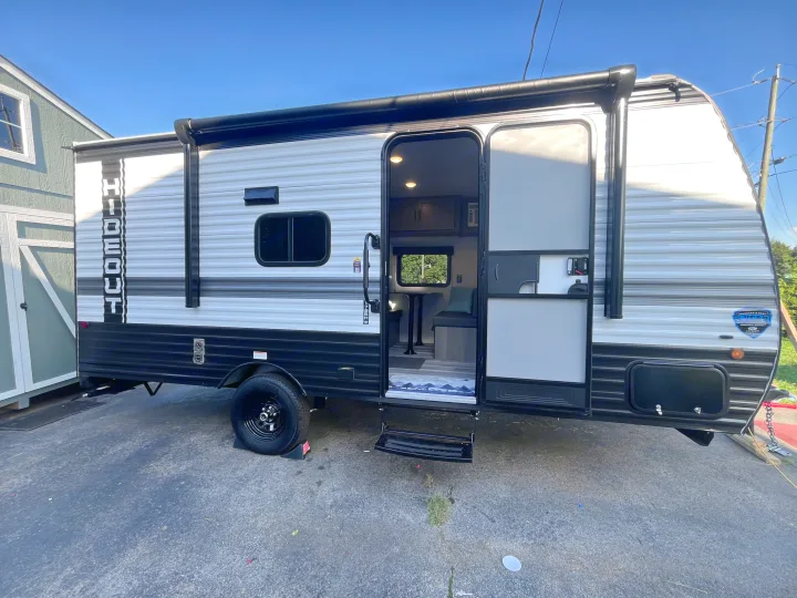 Side view of a "Hideout" travel trailer RV rental with its door open revealing the interior, and an extended awning.. Keystone RV Hideout Sport 2024
