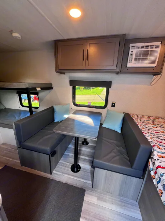Spacious RV rental interior featuring a dinette with benches, bunk beds, and an AC unit. Brightly lit space.. Keystone RV Hideout Sport 2024
