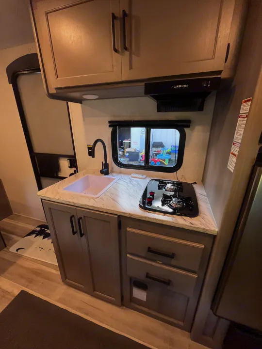 Modern RV rental kitchen with countertop, sink, two-burner stove, and sleek cabinets.. Keystone RV Hideout Sport 2024