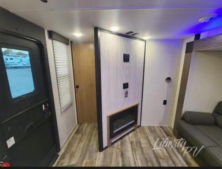 RV rental living space: view of the entry door, entertainment wall with fireplace, and comfy sofa inside a modern travel trailer.. Forest River Cherokee Grey Wolf 2024