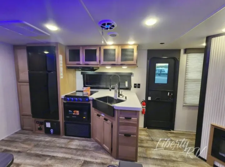 RV rental interior: modern kitchen with stove, fridge, sink, and cool blue ambient lighting.. Forest River Cherokee Grey Wolf 2024