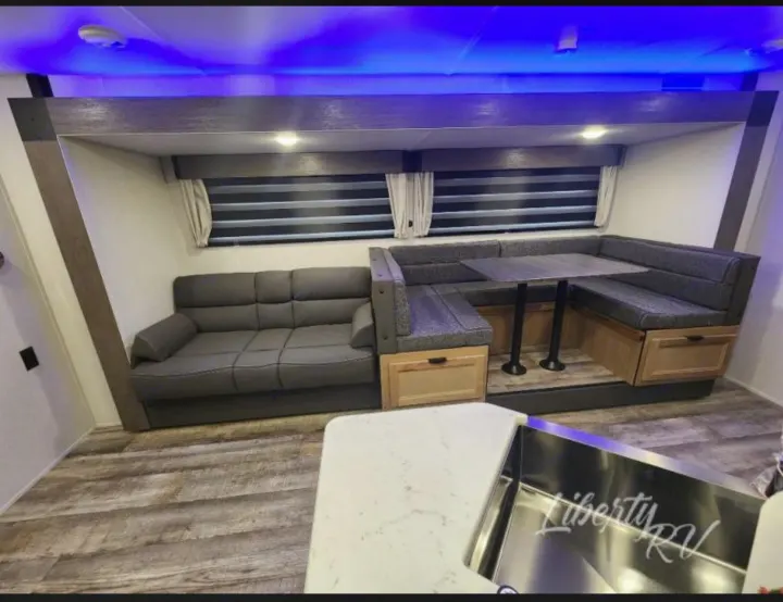 Inside a premium RV rental: inviting sofa, U-shaped dinette with table and storage, plus ambient blue lighting.. Forest River Cherokee Grey Wolf 2024