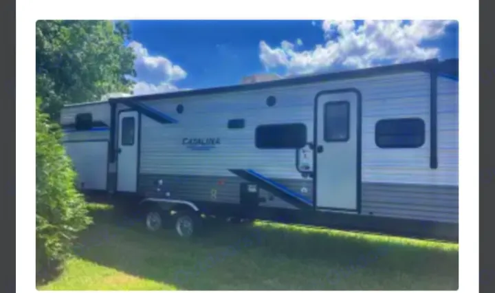 Parked on grass, this grey & white Catalina travel trailer RV rental with blue accents awaits your adventure.. Coachmen Catalina Legacy 323BHDSCK 2022