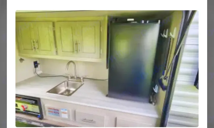 This RV rental features a well-equipped kitchen area with a sink, small refrigerator, and light green cabinets.. Coachmen Catalina Legacy 323BHDSCK 2022