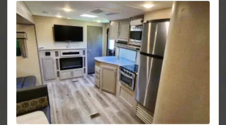 Spacious, modern rv rental interior showcasing living room with TV/fireplace & full kitchen with island, stove, fridge.. Coachmen Catalina Legacy 323BHDSCK 2022