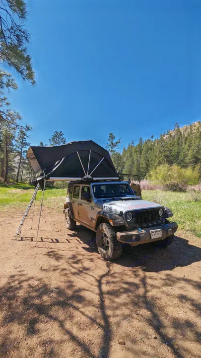 Silver Jeep Wrangler with a rooftop tent deployed, showing its "RENT-RV.CO" branding. An ideal RV rental for outdoor adventures.. Jeep Wrangler 2024