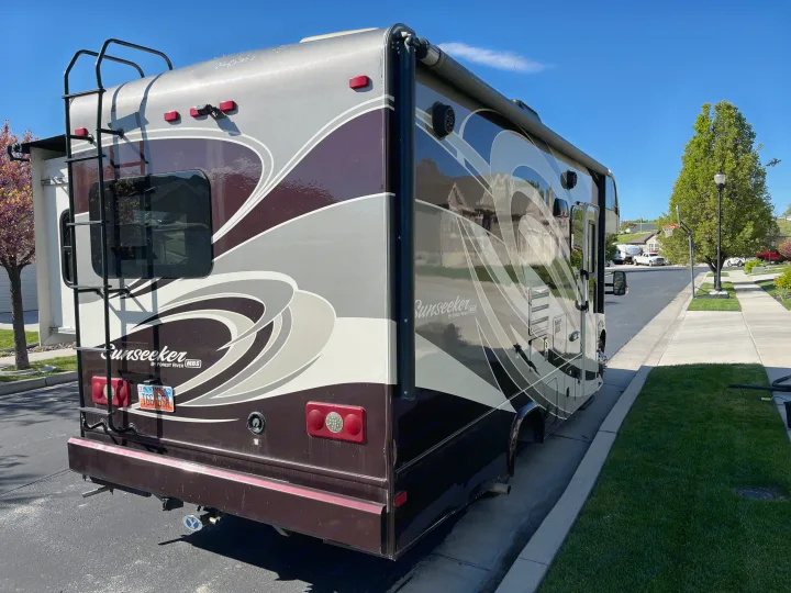 A Sunseeker rv rental, a large motorhome, parked on a sunny day, showcasing its rear ladder and side graphics.. Forest River Sunseeker MBS 2016