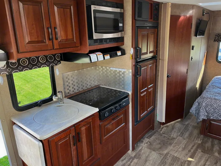 Well-equipped rv rental interior: kitchen with sink, stove, microwave, fridge, and a comfortable bed area.. Forest River Sunseeker MBS 2016