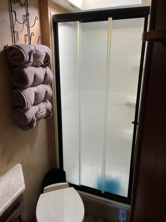 Inside an RV rental: a compact bathroom with a shower, toilet, and rolled towels on a wall rack.. Forest River Sunseeker MBS 2016