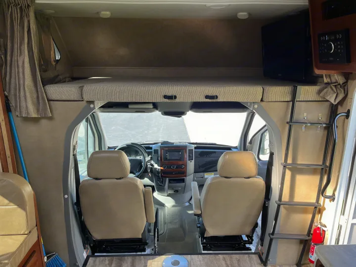 Spacious RV rental interior featuring a cab-over bunk bed, cockpit area, entertainment system, and TV.. Forest River Sunseeker MBS 2016