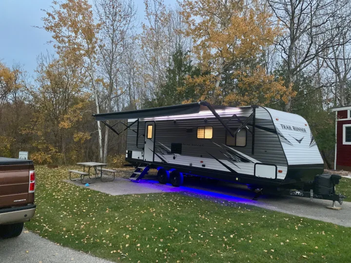 This RV rental, a Trail Runner trailer, glows at a cozy autumn campsite with a picnic table and fallen leaves. Ready for adventure!. Heartland RVs Trail Runner 2021
