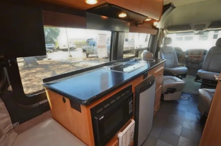 Inside this RV rental: a modern kitchen with sink, microwave, and fridge, plus a spacious living and driver's area.. Winnebago Era 2010