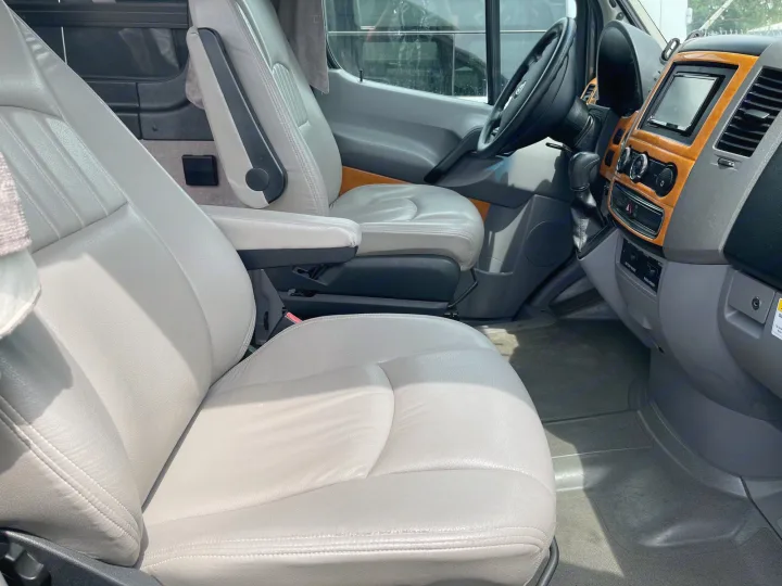 Inside an RV rental: light gray captain's seats, dashboard with wood trim, and steering wheel, showcasing a spacious cabin.. Winnebago Era 2010