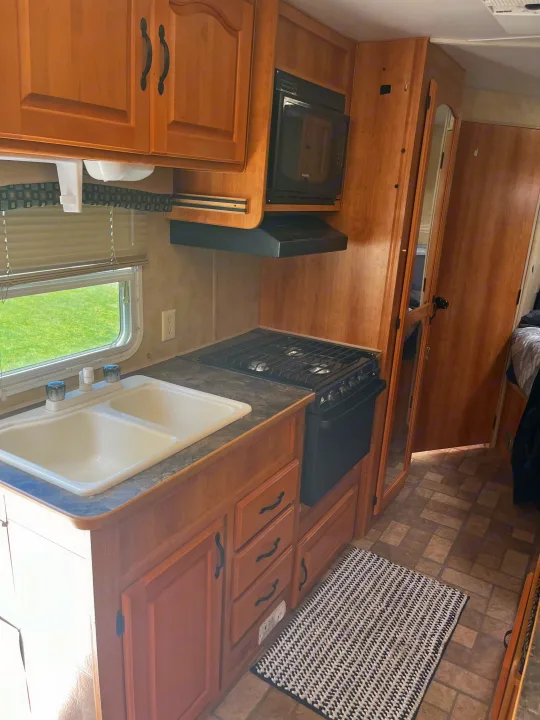 Well-equipped RV rental kitchen featuring light wood cabinets, double sink, stove, microwave, and window view, ideal for travel.. Coachmen SportsMaster 2008