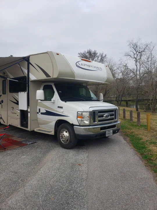 Explore nature with this RV rental! A Class C motorhome by a river, wooden bridge, and bare trees for your next escape.. Forest River Coachmen Leprechaun 2015