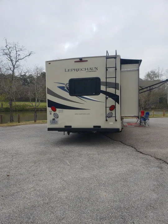 RV rental parked by water with awning & chairs. Texas plate. Ideal for outdoor adventures & travel.. Forest River Coachmen Leprechaun 2015