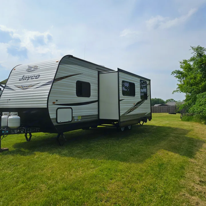 Jayco travel trailer RV rental, with a slide-out extended, parked on vibrant green grass under a bright sky.. Jayco Jay Flight SLX8 2020