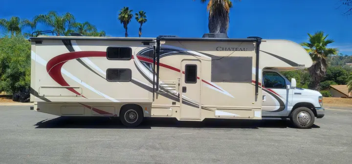 Side view of a tan and maroon Class C RV rental, parked outdoors on a clear day. Ready for your next road trip!. Thor Chateau 2018