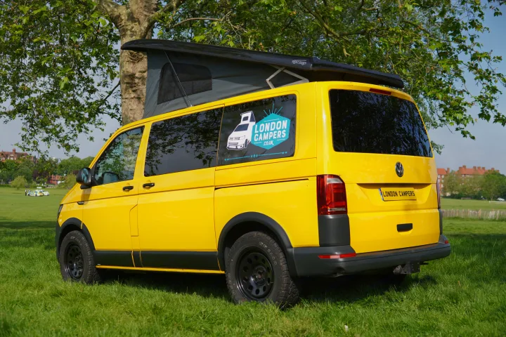 A bright yellow campervan, a London Campers RV rental, is parked on green grass with its pop-top roof extended.. Volkswagen T6 2017