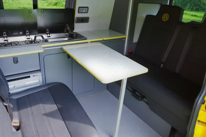 Inside an RV rental: Modern kitchenette, adaptable table, and comfortable black seating, ideal for road trips.. Volkswagen T6 2017