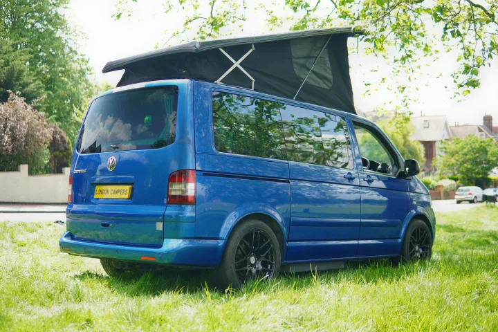A bright blue Volkswagen camper van, with its pop-top roof extended, is parked on sunlit grass, ideal for an RV rental.. Volkswagen Other 2006