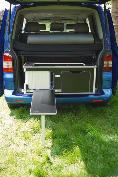 RV rental ready: Blue camper van's tailgate open, showing a pull-out kitchen, bed, and outdoor table on grass.. Volkswagen Other 2006