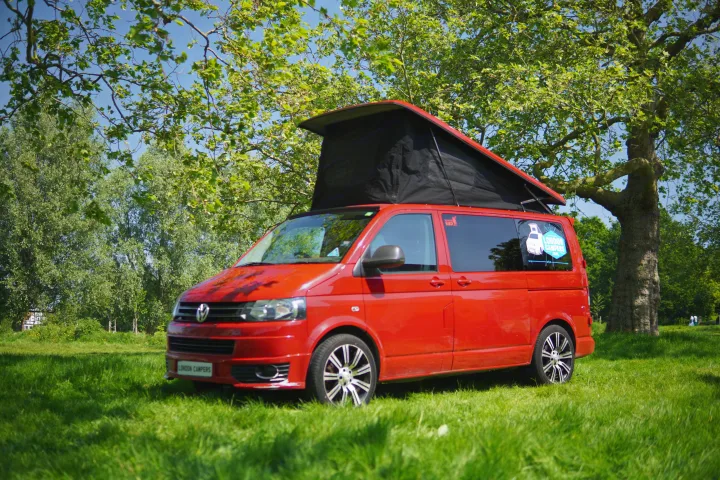 Vibrant red VW campervan with pop-top roof, parked on lush grass. Ideal for your next RV rental adventure.. Volkswagen T5 premium camper 2011