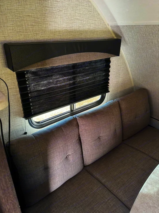 Cozy RV rental interior with a comfortable gray sofa, black privacy blinds on the window, and textured walls for travel.. Braxton Creek Bushwhacker Plus 2022