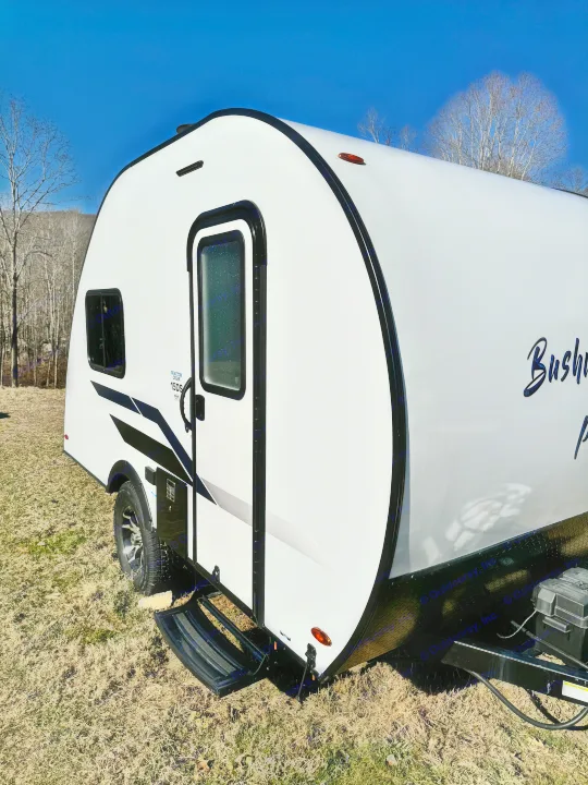 Sleek white travel trailer, an ideal rv rental camper, parked on dry grass under a bright blue sky with distant bare trees.. Braxton Creek Bushwhacker Plus 2022