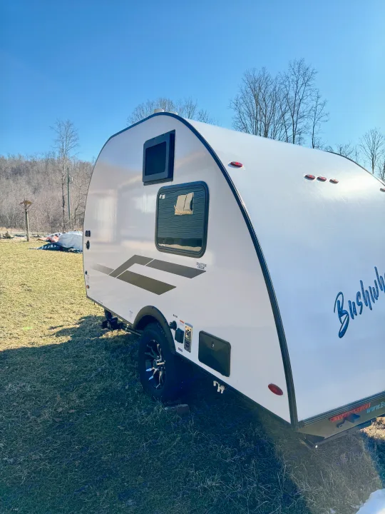 Compact white Braxton Creek Bushwhacker teardrop RV rental on grass under blue sky, ready for outdoor adventures.. Braxton Creek Bushwhacker Plus 2022