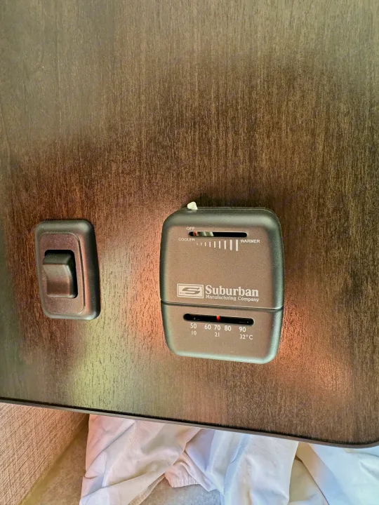 Suburban RV thermostat and light switch on wood panel wall, set to 70°F/21°C. Essential for rv rental climate control.. Braxton Creek Bushwhacker Plus 2022