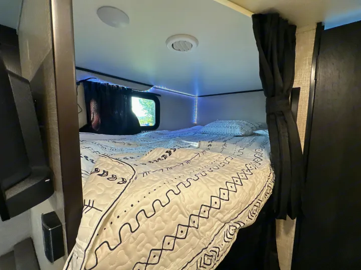 Inside an RV rental: a cozy sleeping nook with a patterned comforter, window, and modern LED lighting.. Jayco Jay Flight 2023