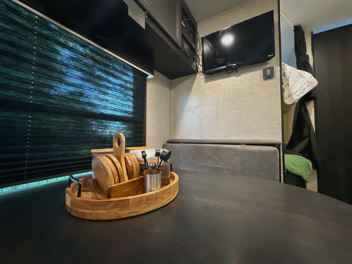 Cozy RV rental interior: dining table with wood caddy, window blinds, TV, and comfortable dinette seating.. Jayco Jay Flight 2023