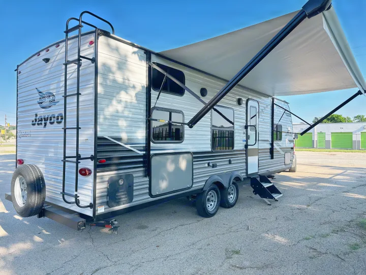A sleek Jayco travel trailer, ideal for RV rental, with an extended awning, rear ladder, and spare tire shown.. Jayco Jay Flight 2023